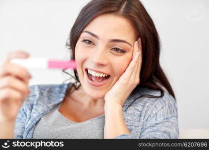 pregnancy, fertility, maternity, emotions and people concept - happy smiling woman looking at pregnancy test at home