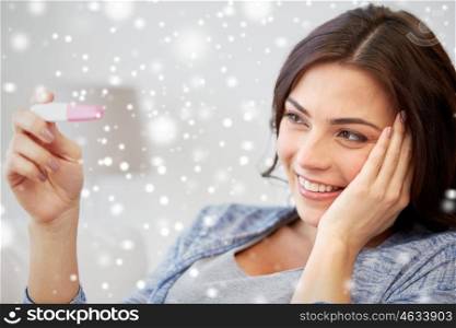pregnancy, fertility, maternity, winter and people concept - happy smiling woman looking at pregnancy test at home over snow