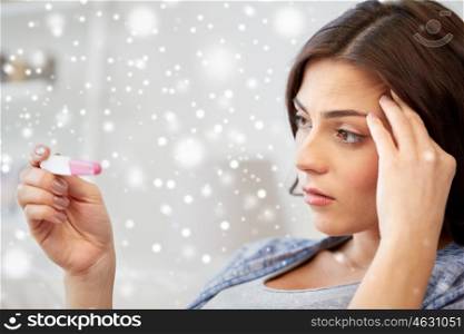 pregnancy, fertility, maternity, winter and people concept - sad unhappy woman looking at pregnancy test at home over snow