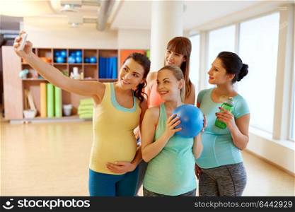 pregnancy, fitness and healthy lifestyle concept - group of happy pregnant women with sports stuff taking selfie by smartphone in gym. pregnant women taking selfie by smartphone in gym