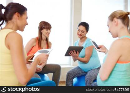 pregnancy, fitness and technology concept - group of happy pregnant women with tablet pc computers and smartphone sitting on exercise balls in gym. happy pregnant women with tablet pc in gym. happy pregnant women with tablet pc in gym