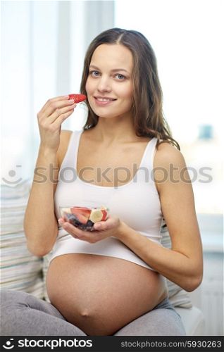 pregnancy, food, healthy eating, people and expectation concept - happy pregnant woman eating fruits at home