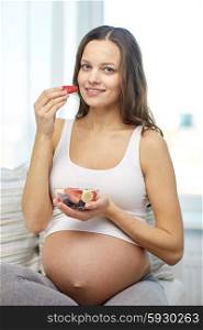 pregnancy, food, healthy eating, people and expectation concept - happy pregnant woman eating fruits at home