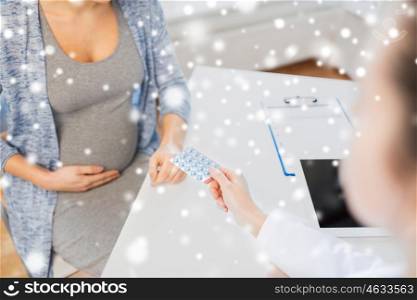 pregnancy, gynecology, medicine, health care and people concept - close up of gynecologist doctor giving pills to pregnant woman at hospital over snow