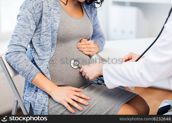 pregnancy, gynecology, medicine, health care and people concept - close up of gynecologist doctor with stethoscope listening to pregnant woman baby heartbeat at hospital