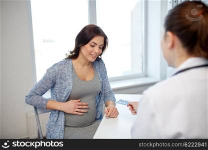 pregnancy, gynecology, medicine, health care and people concept - smiling gynecologist doctor giving pills to pregnant woman meeting at hospital