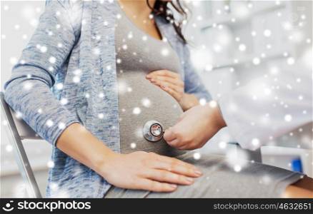 pregnancy, gynecology, medicine, healthcare and people concept - close up of obstetrician doctor with stethoscope listening to pregnant woman baby heartbeat at hospital over snow