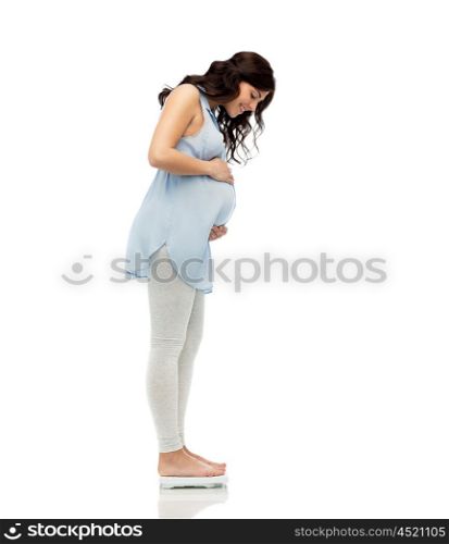 pregnancy, health care and people concept - happy pregnant woman measuring weight on scales over white background