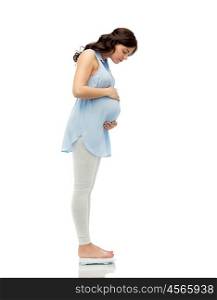 pregnancy, health care and people concept - happy pregnant woman measuring weight on scales over white background