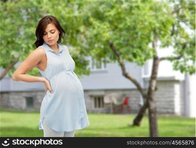 pregnancy, health, people and expectation concept - pregnant woman touching her back and suffering from backache over summer garden and house background