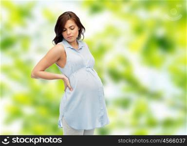 pregnancy, health, people and expectation concept - pregnant woman touching her back and suffering from backache over green natural background