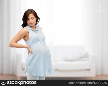 pregnancy, health, people and expectation concept - pregnant woman touching her back and suffering from backache over home living room background