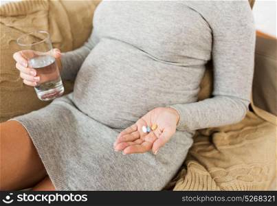 pregnancy, healthcare, people and medicine concept - close up of pregnant woman with pills and water at home. close up of pregnant woman with pills at home
