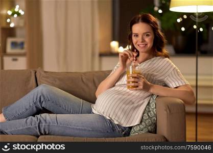 pregnancy, healthy eating and people concept - happy smiling pregnant woman drinking juice or smoothie from disposable cup with paper straw at home. happy pregnant woman drinking juice at home