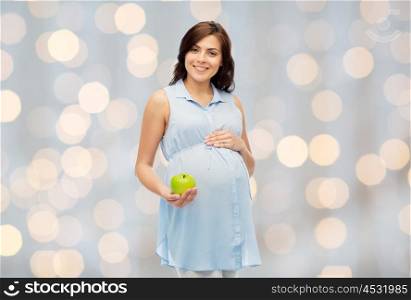 pregnancy, healthy eating, food and people concept - happy pregnant woman holding green apple over holidays lights background