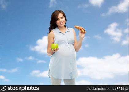 pregnancy, healthy eating, junk food and people concept - happy pregnant woman choosing between green apple and croissant over blue sky and clouds background