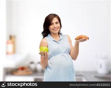 pregnancy, healthy eating, junk food and people concept - happy pregnant woman choosing between green apple and croissant over kitchen background