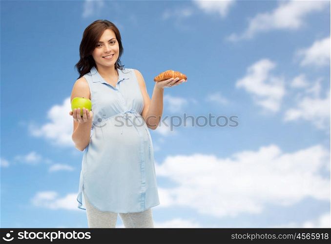 pregnancy, healthy eating, junk food and people concept - happy pregnant woman choosing between green apple and croissant over blue sky and clouds background