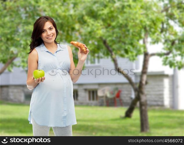 pregnancy, healthy eating, junk food and people concept - happy pregnant woman choosing between green apple and croissant over summer garden and house background