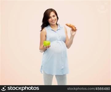 pregnancy, healthy eating, junk food and people concept - happy pregnant woman choosing between green apple and croissant over beige background