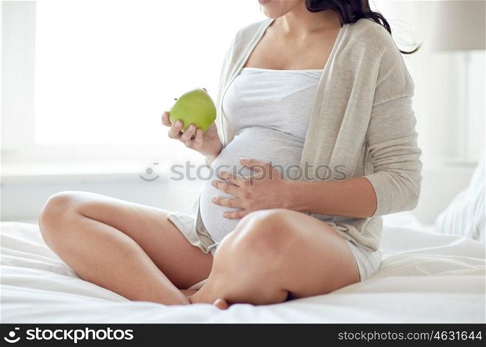 pregnancy, healthy food and people concept - close up of happy pregnant woman eating green apple at home