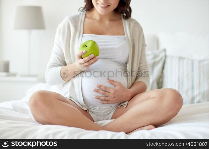 pregnancy, healthy food and people concept - close up of happy pregnant woman eating green apple at home