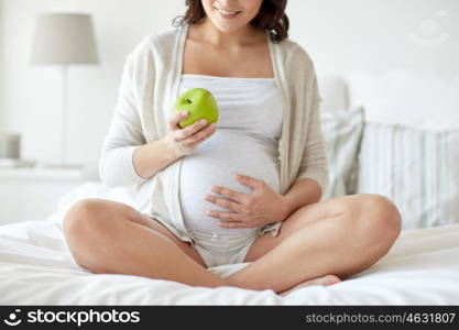 pregnancy, healthy food and people concept - close up of happy pregnant woman eating green apple at home