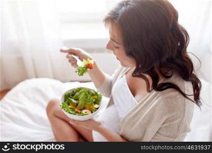 pregnancy, healthy food and people concept - close up of happy pregnant woman eating vegetable salad for breakfast in bed at home