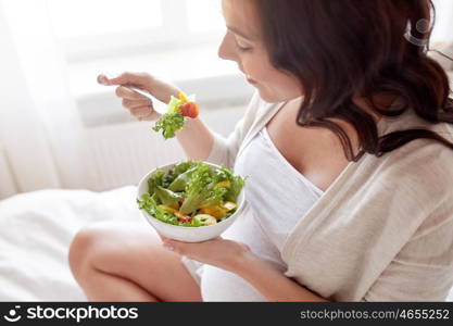 pregnancy, healthy food and people concept - close up of happy pregnant woman eating vegetable salad for breakfast in bed at home