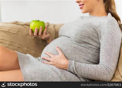 pregnancy, healthy food and people concept - close up of happy pregnant woman eating green apple at home. happy pregnant woman eating green apple at home