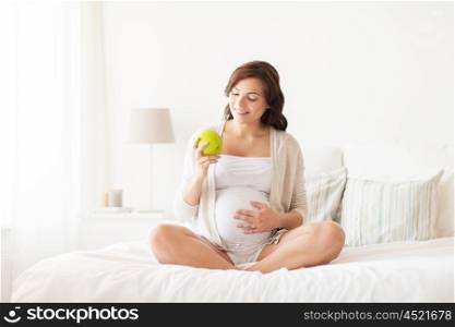 pregnancy, healthy food and people concept - happy pregnant woman eating green apple at home