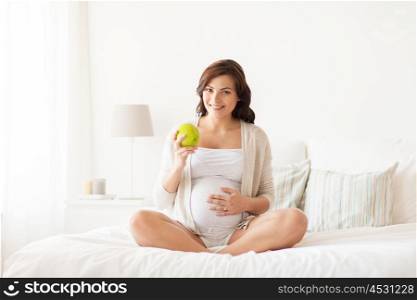 pregnancy, healthy food and people concept - happy pregnant woman eating green apple at home