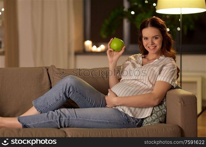 pregnancy, healthy food and people concept - happy smiling pregnant woman eating green apple at home. happy pregnant woman with green apple at home