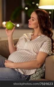 pregnancy, healthy food and people concept - happy smiling pregnant woman eating green apple at home. happy pregnant woman with green apple at home