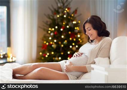 pregnancy, holidays and expectation concept - happy pregnant woman lying on bed and touching her belly at home over christmas tree lights background. happy pregnant woman at home on christmas