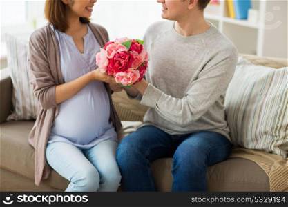 pregnancy, holidays and people concept - close up of happy husband giving flowers to his pregnant wife at home. close up of man giving flowers to pregnant wife