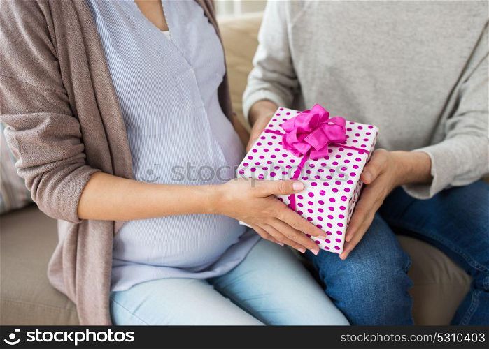 pregnancy, holidays and people concept - close up of husband giving present to his pregnant wife at home. close up of man giving present to pregnant wife