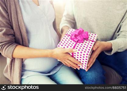 pregnancy, holidays and people concept - close up of husband giving present to his pregnant wife at home. close up of man giving present to pregnant wife