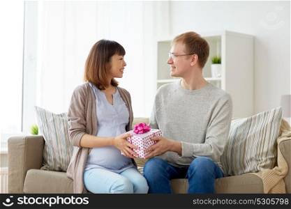 pregnancy, holidays and people concept - happy husband giving birthday present to his pregnant wife at home. husband giving birthday present to pregnant wife