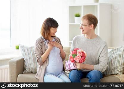 pregnancy, holidays and people concept - happy husband giving flowers and birthday present to his pregnant wife at home. happy husband giving present to his pregnant wife