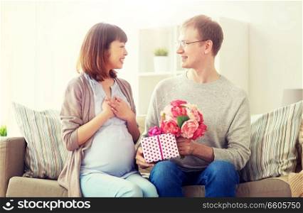 pregnancy, holidays and people concept - happy husband giving flowers and birthday present to his pregnant wife at home. happy husband giving present to his pregnant wife