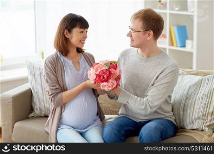 pregnancy, holidays and people concept - happy husband giving flowers to his pregnant wife for birthday at home. happy husband giving flowers to his pregnant wife