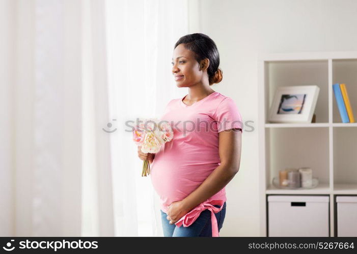 pregnancy, holidays and people concept - happy pregnant african american woman with flowers looking through window at home. happy african american pregnant woman with flowers