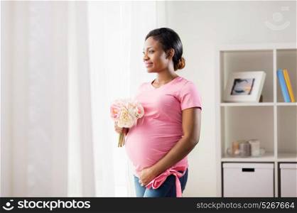 pregnancy, holidays and people concept - happy pregnant african american woman with flowers looking through window at home. happy african american pregnant woman with flowers