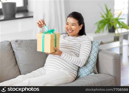 pregnancy, holidays and people concept - happy smiling pregnant asian woman with gift box sitting on sofa at home. happy pregnant woman with gift box at home