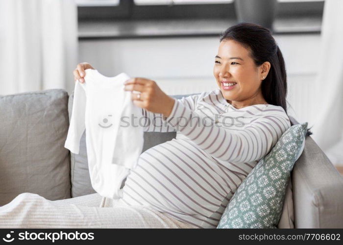 pregnancy, holidays and people concept - happy smiling pregnant asian woman with baby&rsquo;s bodysuit at home. happy pregnant woman with baby&rsquo;s bodysuit at home