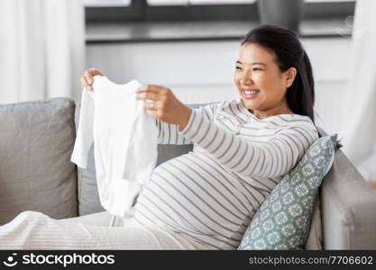 pregnancy, holidays and people concept - happy smiling pregnant asian woman with baby&rsquo;s bodysuit at home. happy pregnant woman with baby&rsquo;s bodysuit at home