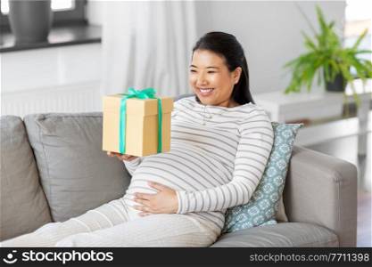 pregnancy, holidays and people concept - happy smiling pregnant asian woman with gift box sitting on sofa at home. happy pregnant woman with gift box at home
