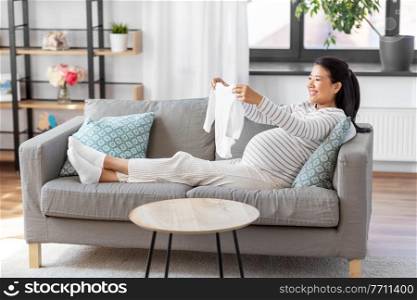 pregnancy, holidays and people concept - happy smiling pregnant asian woman with baby’s bodysuit at home. happy pregnant woman with baby’s bodysuit at home