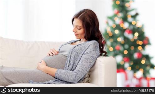pregnancy, holidays, people and expectation concept - happy pregnant woman lying on sofa over christmas tree background